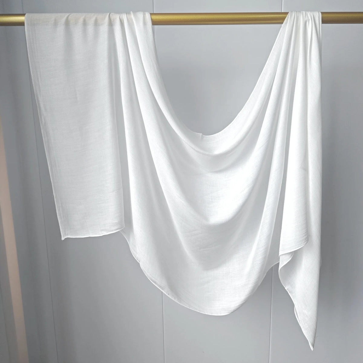 Foulard modal uni blanc drapé sur une tige dorée.