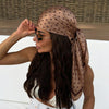 A woman wearing a brown polka dot silk scarf tied around her hair and neck.