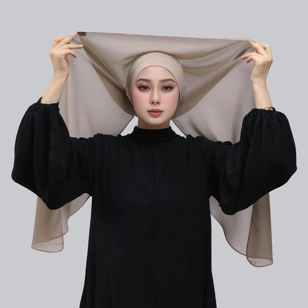 A woman models an elegant beige chiffon hijab shawl draped over her head and shoulders, paired with a black high-neck top.