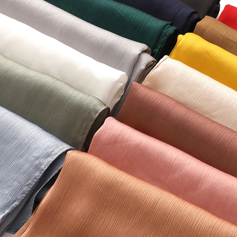 Eine Sammlung gefalteter, hochwertige Satin-Crinkle-Hijabs in verschiedenen Farben wie Grün, Beige, Gelb und Pink.