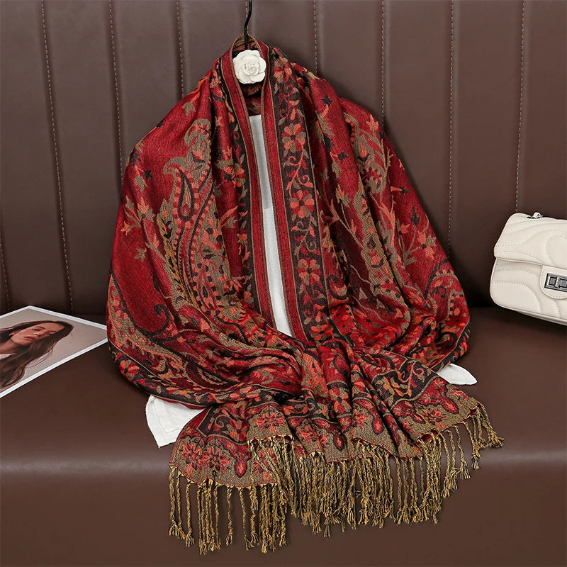 Pañuelo pashmina de lujo rojo y dorado, drapeado sobre una superficie de cuero marrón.