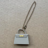 Una cadena de plata unida a un accesorio de bolso de cuero gris sobre un fondo neutro.