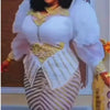 A woman wearing a white and gold sequin African party dress with puffy sleeves and a striped skirt.