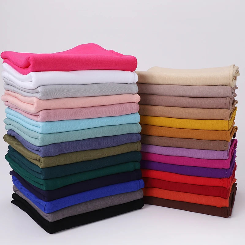 Ein Stapel von Jersey-Hijab-Schals in verschiedenen Farben wie rosa, weiß, grau, blau, grün und lila.