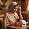 A woman wearing a beige hijab with a black crown, looking down while applying it.