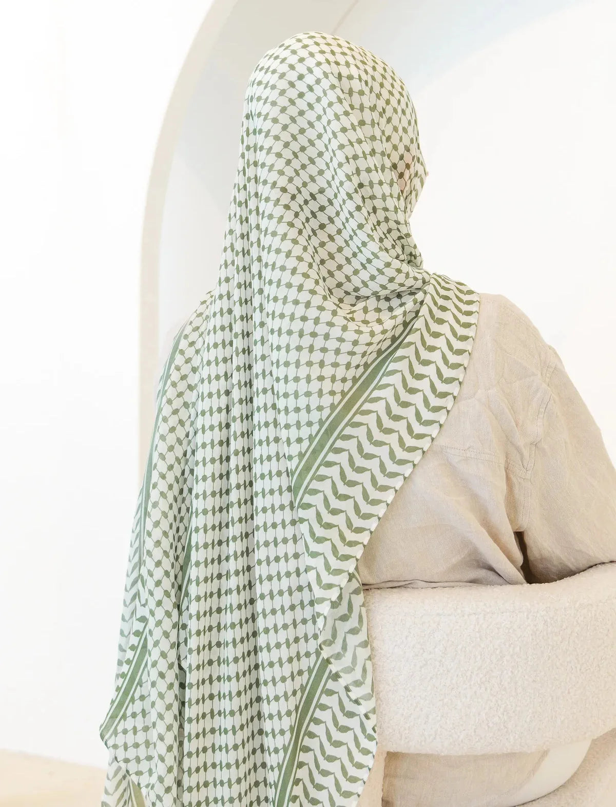 Una mujer vistiendo un elegante hijab de gasa con estampado verde y blanco cubriendo su cabeza y cuello.