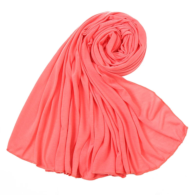 Ein leuchtend korallenrosa Baumwoll-Jersey-Schal, gerollt und drapiert, zeigt seine weiche Textur.