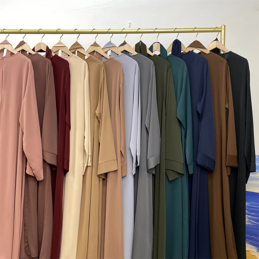 Una estantería de elegantes abayas de encaje en tonos tierra y azules profundos colgadas en un percha de madera.