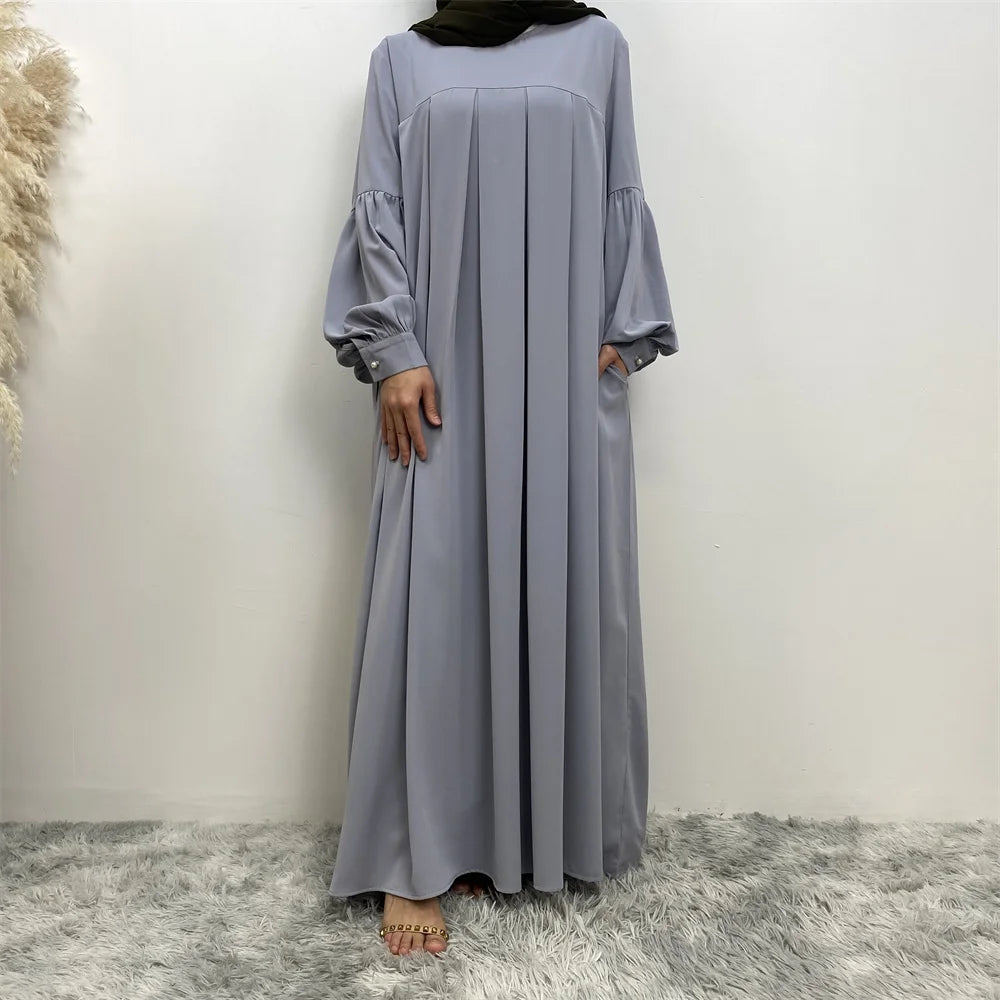 Eine Frau trägt ein langes, fließendes, hellgraues islamisches Kleid mit weiten Ärmeln und einem schwarzen Hijab.