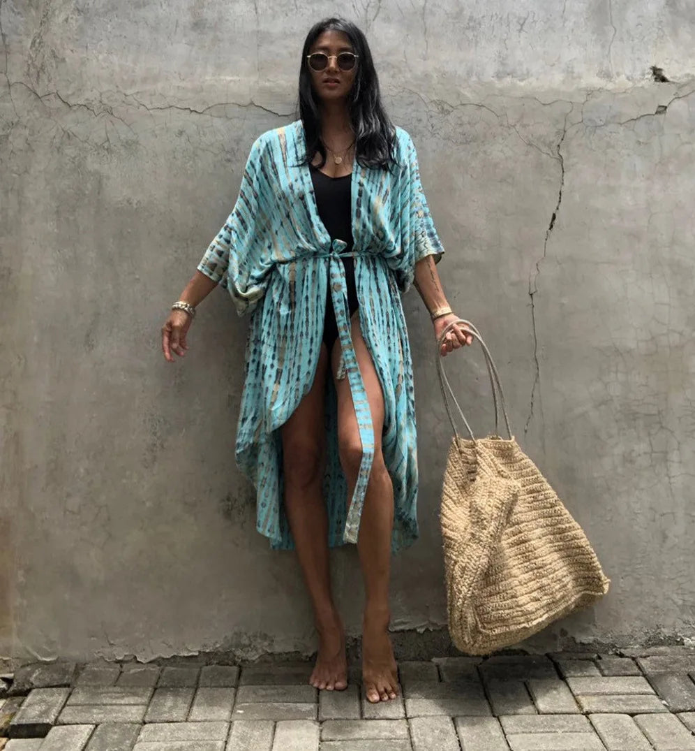 Eine Frau in einem hellblauen gemusterten Kimono-Überkleid vor einer grauen Betonwand.