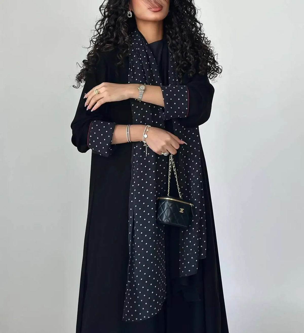 Eine Frau trägt ein elegantes schwarzes Polka-Dot-Abaya-Cardigan-Kleid mit dunkler Kleidung und goldenen Schmuck.