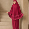 Eine Frau trägt ein mehrlagiges Spitzen-Khimar-Abaya-Set in tiefem Weinrot in einer architektonischen Umgebung.
