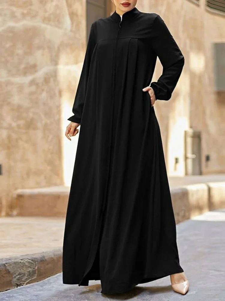 Une femme portant une élégante robe longue noire ample à col montant, debout à l'extérieur.