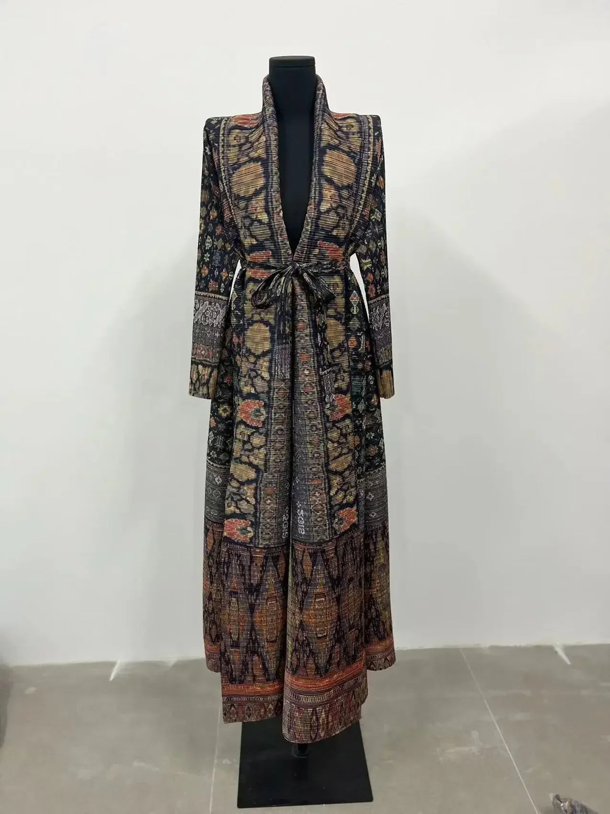Manteau trench à manches longues plissé à motif sombre, exposé sur un mannequin noir.