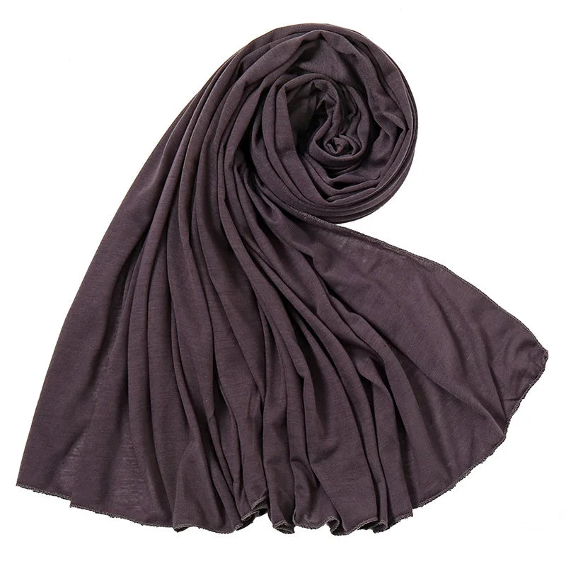 Un foulard hijab en jersey de coton violet foncé roulé et drapé, montrant sa texture douce.