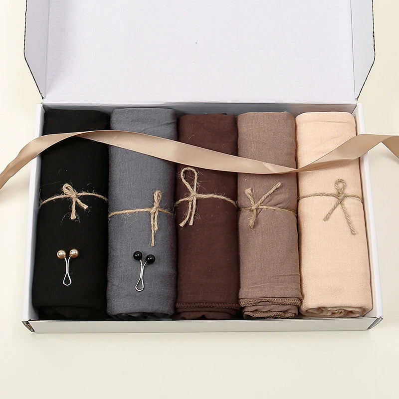 Une boîte contenant neuf foulards de hijab moulants roulés de couleurs unies noirs, gris, marron, beige et tan.