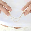 Un par de manos sosteniendo un juego de pinzas magnéticas para ropa con delicadas cadenas de tono dorado.