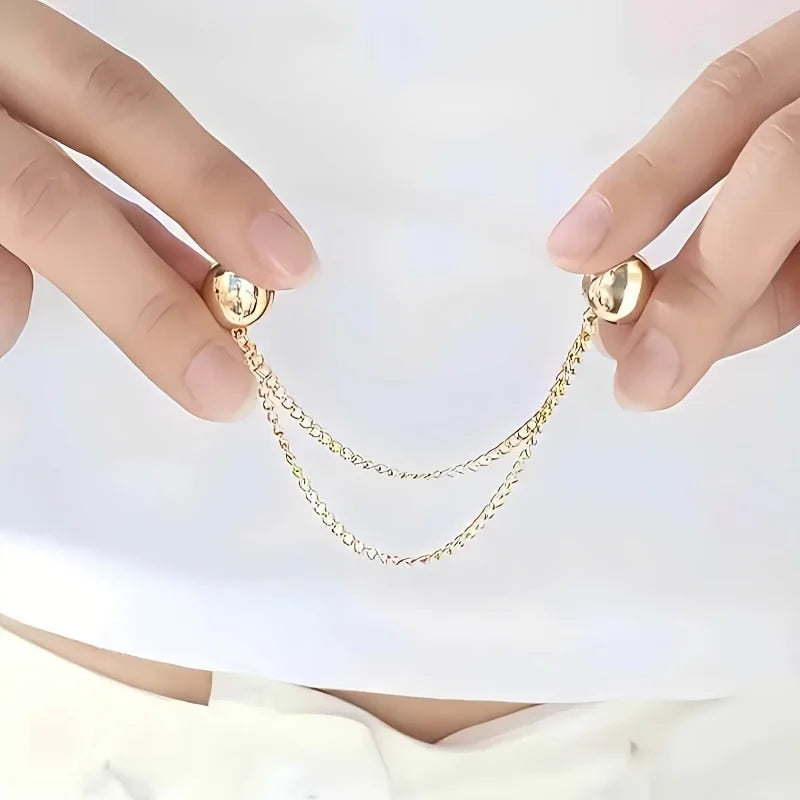 Un par de manos sosteniendo un juego de pinzas magnéticas para ropa con delicadas cadenas de tono dorado.