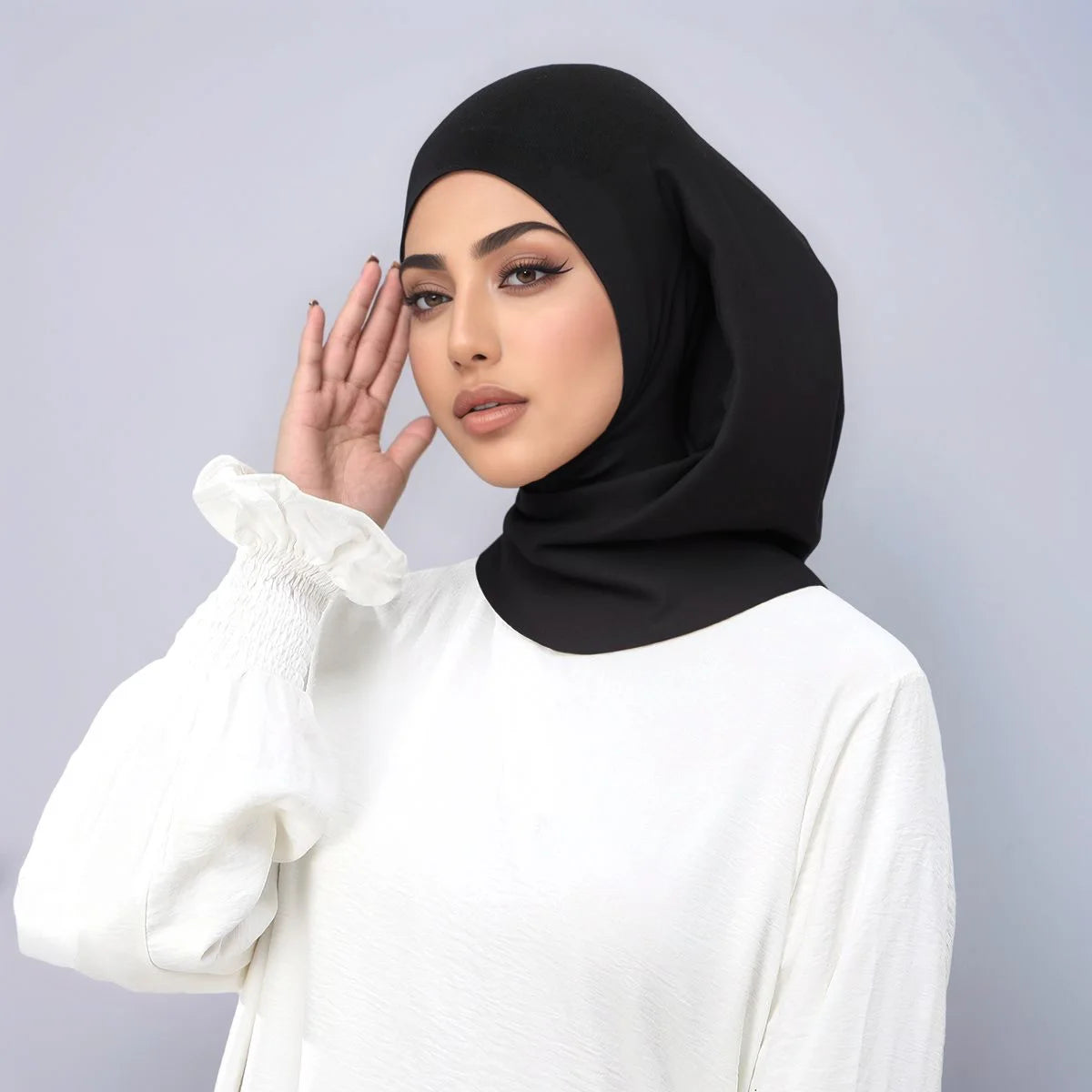 Eine Frau trägt ein schwarzes Instant-Turban-Hijab, ein Undercap-Bonnet und ein weißes Langarm-Oberteil.