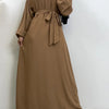 Eine Frau trägt eine lange, erdtonige marokkanische Kaftan-Abaya mit voluminösen Ärmeln und einem gebundenen Bund.