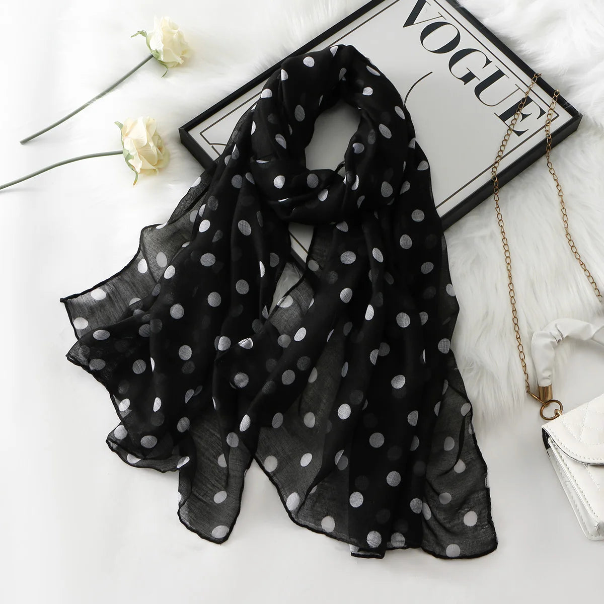 Schleierartige schwarze Chiffon-Schal mit weißen Polkadotierungen auf weißem Stoff neben einer Vogue-Magazin.