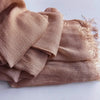 Une pile de foulards hijab en coton viscose beige doux avec pompons, pliés sur une surface blanche.