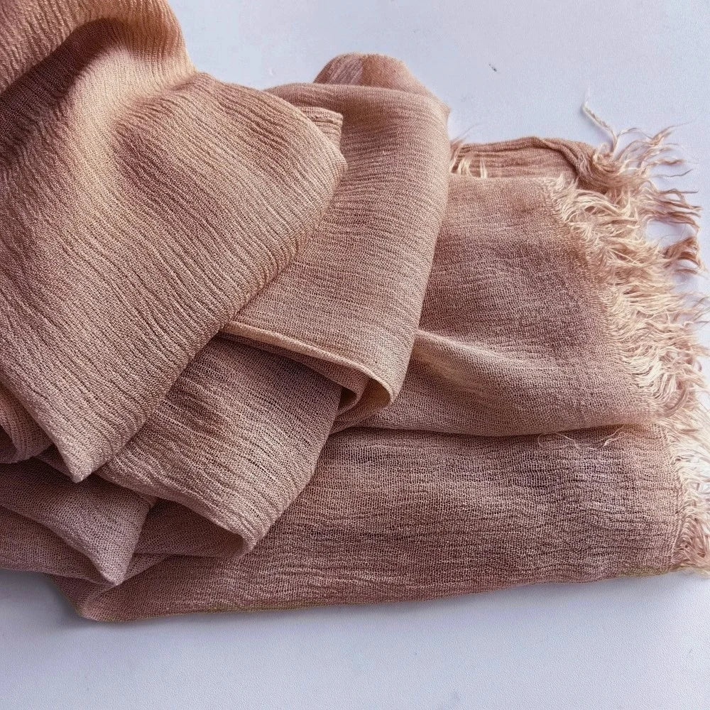 Une pile de foulards hijab en coton viscose beige doux avec pompons, pliés sur une surface blanche.