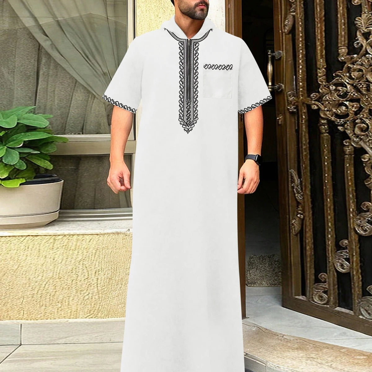 A white Moroccan men's ethnic thobe with a stand collar and black embroidery, displayed indoors.