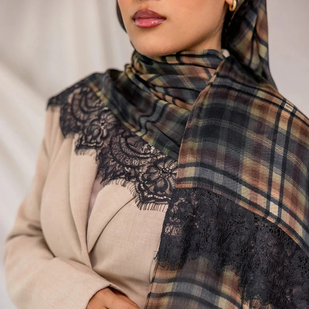 A close-up of a woman wearing a premium printed modal plaid hijab scarf with black lace detailing and earth tones.
