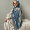 Una mujer vistiendo un pañuelo hijab con estampado de acuarela azul y gris y una blusa blanca.
