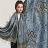 Eine Frau modelliert einen eleganten blau-goldenen Paisley-Viskose-Hijabschal über ihre Schulter.