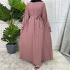 Fließendes, staubrosafarbenes Maxi-Abaya für Frauen vor einer weißen Paneelwand.