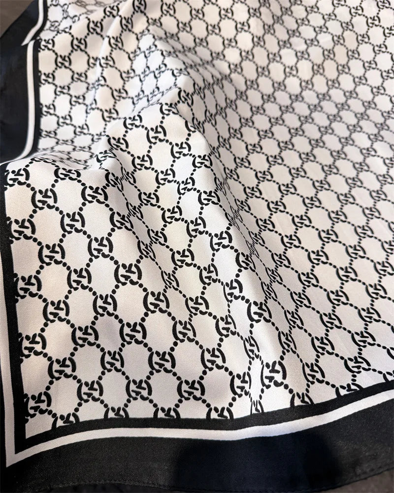 Nahaufnahme eines weißen Seidenschals mit schwarzem geometrischem Vierblattmuster, drapiert im Stoff.