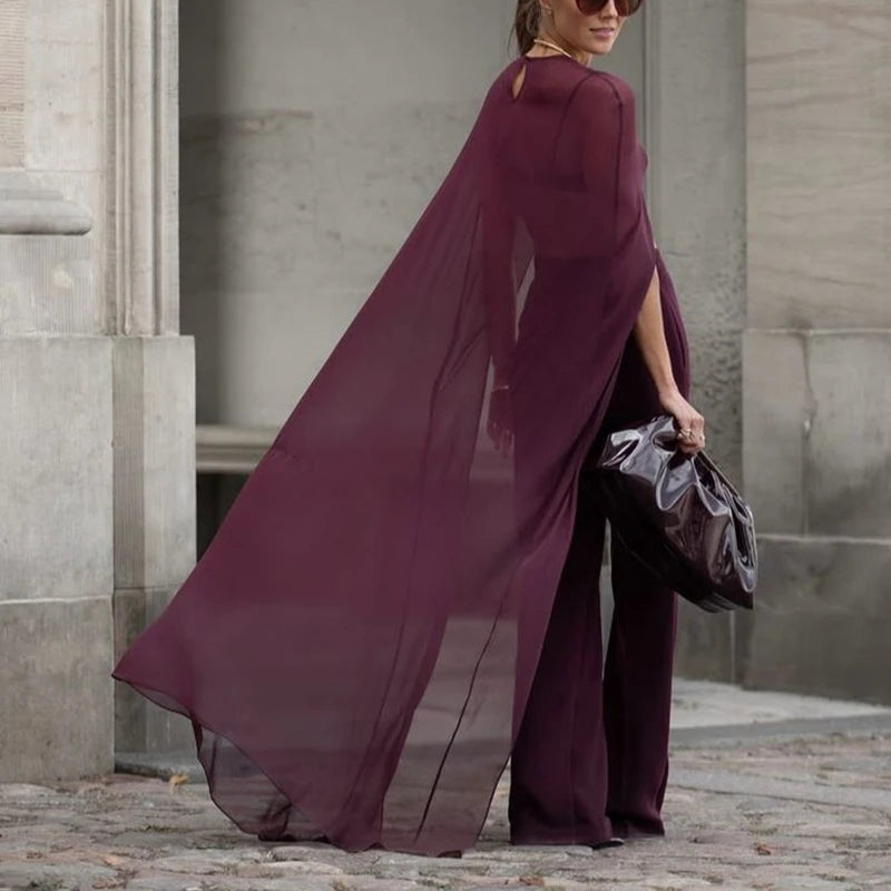 A woman wearing an elegant sheer mesh poncho cape in deep plum color standing outdoors.