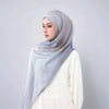 Eine Frau trägt einen hellblauen Aquarell-druckenbestickten Leinen-Baumwoll-Hijab-Schal über einem weißen Oberteil.