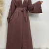 Eine Frau trägt ein fließendes, offenes Abaya-Kaftan in staubrosa Farbe mit einem weißen Hijab.