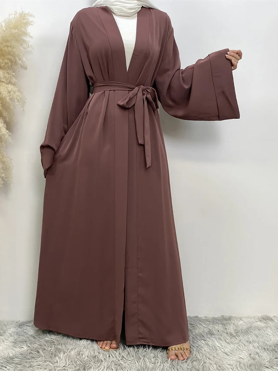 Eine Frau trägt ein fließendes, offenes Abaya-Kaftan in staubrosa Farbe mit einem weißen Hijab.
