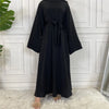 Eine elegante schwarze Maxi-Abaya für Frauen wird vor einer weißen Paneelwand präsentiert.
