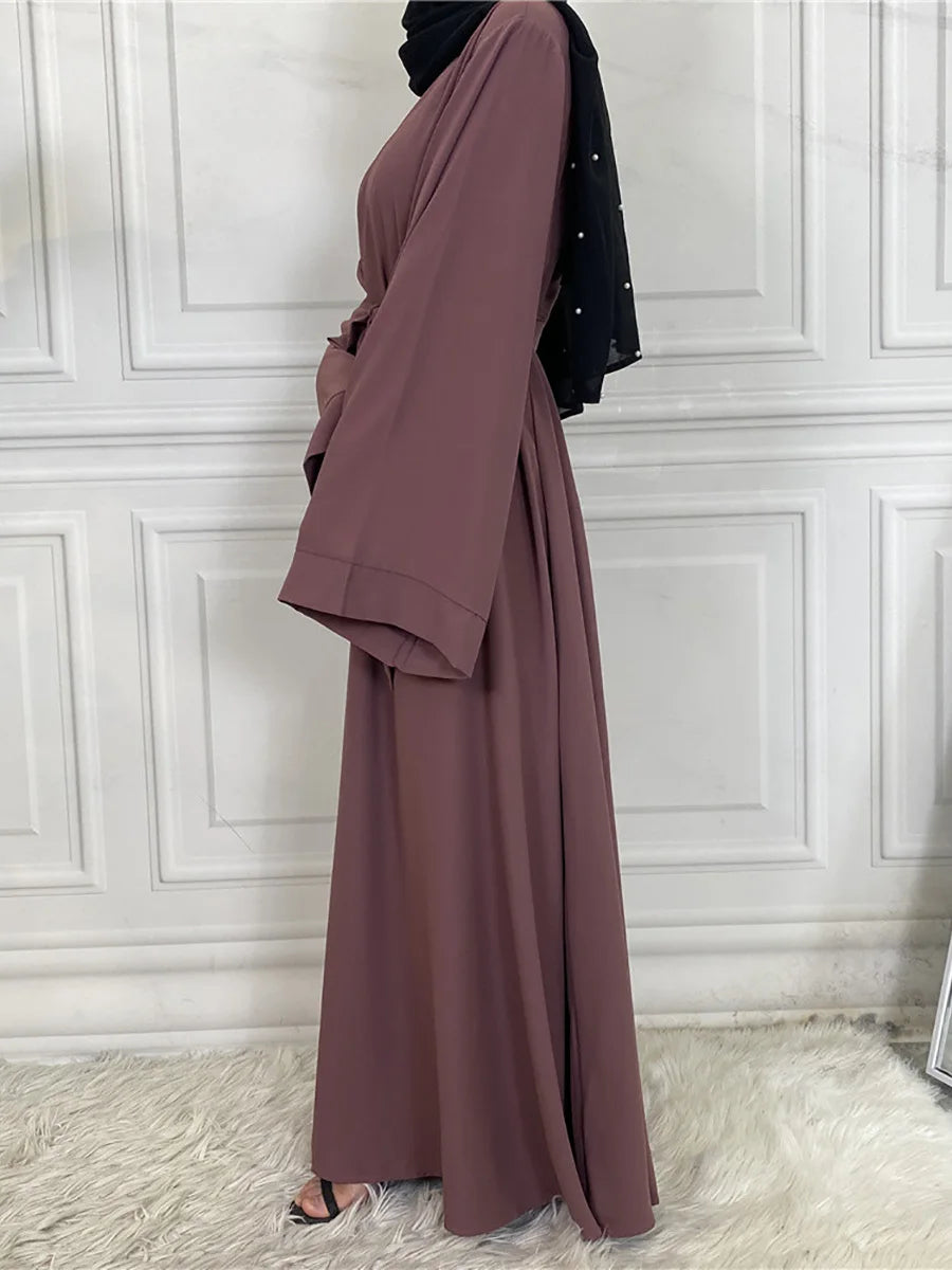 Eine Frau trägt eine elegante mauve Abaya mit schwarzen Akzenten, steht in einem gut beleuchteten Raum.
