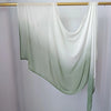 Pañuelo de hijab de algodón rayón con degradado verde claro colgando en una varilla de madera.