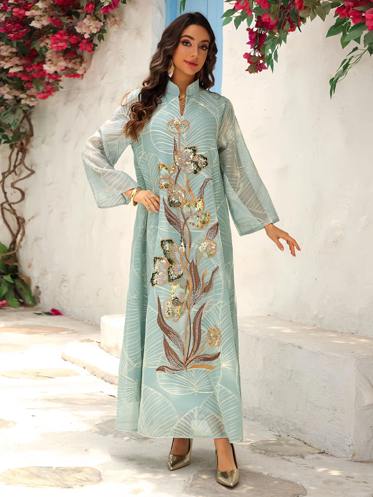 Eine Frau modelliert eine hellblaue Pailletten-bestickte Abaya mit goldenen Blumenverzierungen im Freien.