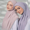 Eine Frau trägt einen eleganten, hellrosa Modal-Jersey-Hijab und ein weißes Oberteil und blickt in die Kamera.