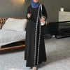 Eine Frau in einem eleganten schwarzen Abaya-Kleid mit weißer Spitze und weißem Träger, steht drinnen.