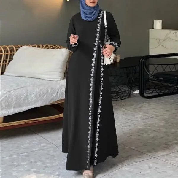 A woman wearing an elegant black abaya dress with white lace detailing and a white strap, standing indoors.