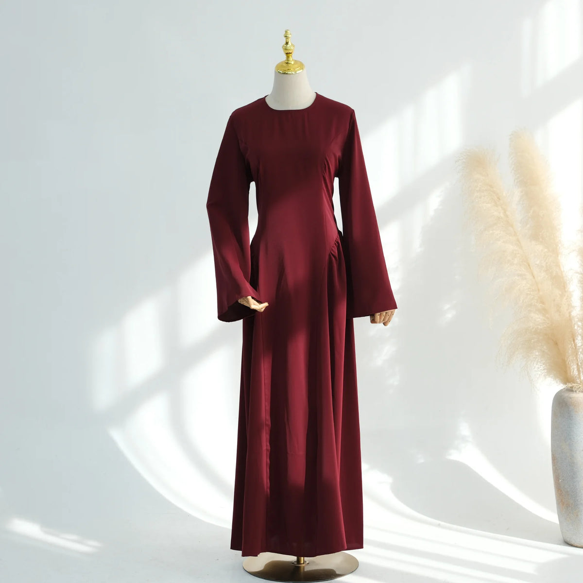 Una abaya de manga larga color granate exhibida en un maniquí contra un fondo claro.
