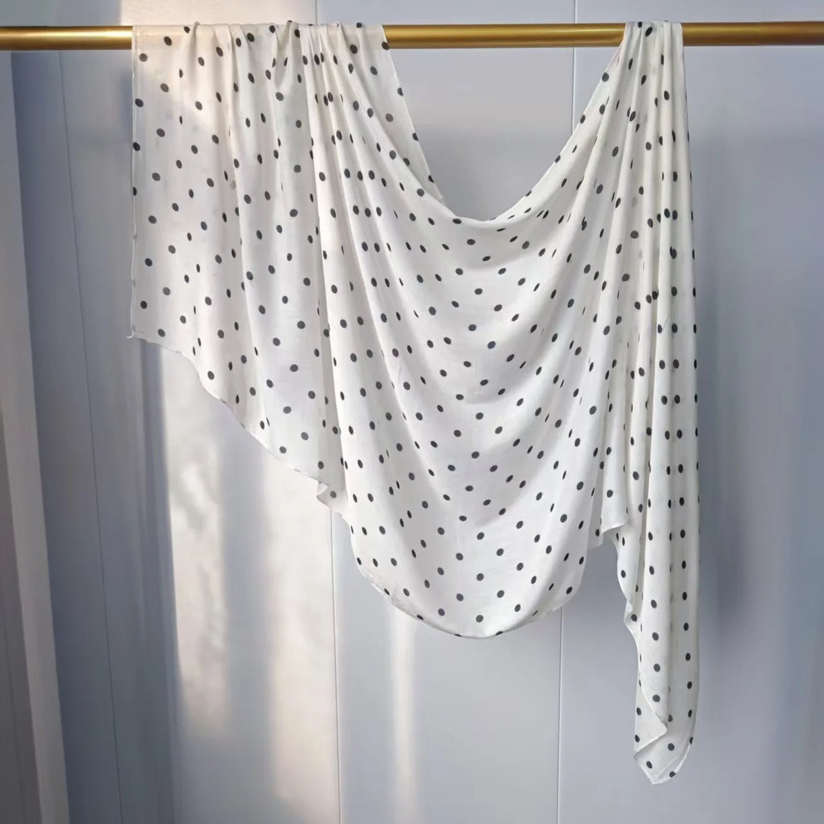 Weißer Hijab-Schal mit schwarzen Polka Dots über einem Holzhaken.