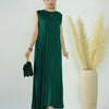 A woman models a flowing, emerald green modest abaya dress with black accessories against a white background.