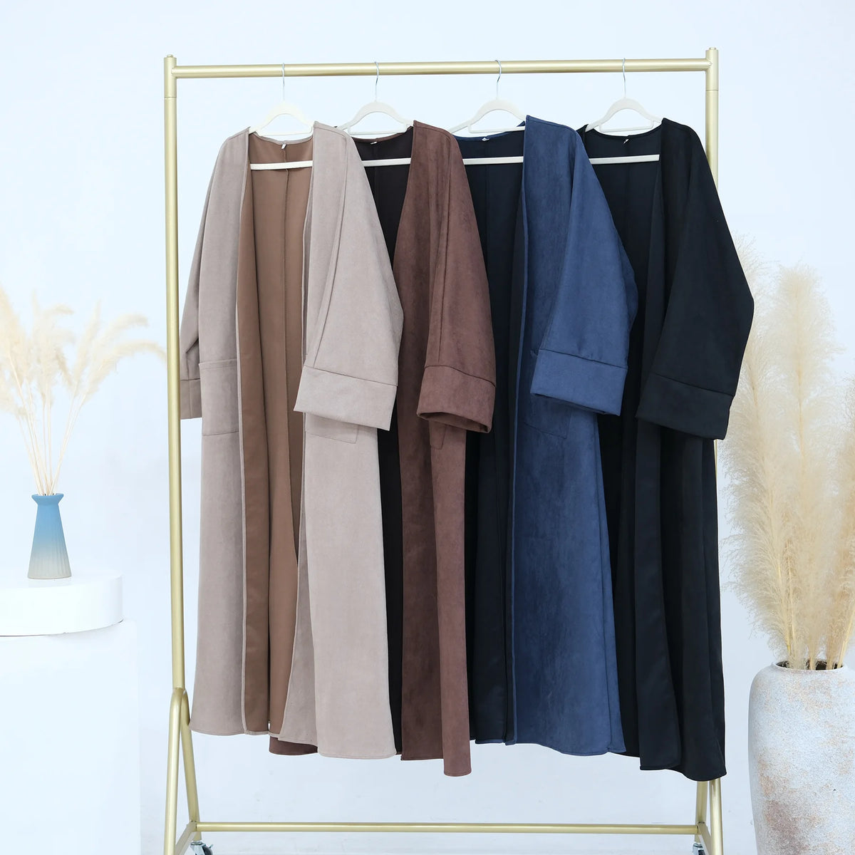 A display of elegant women's abaya trench coats in various neutral and dark colors hanging on a gold rack.