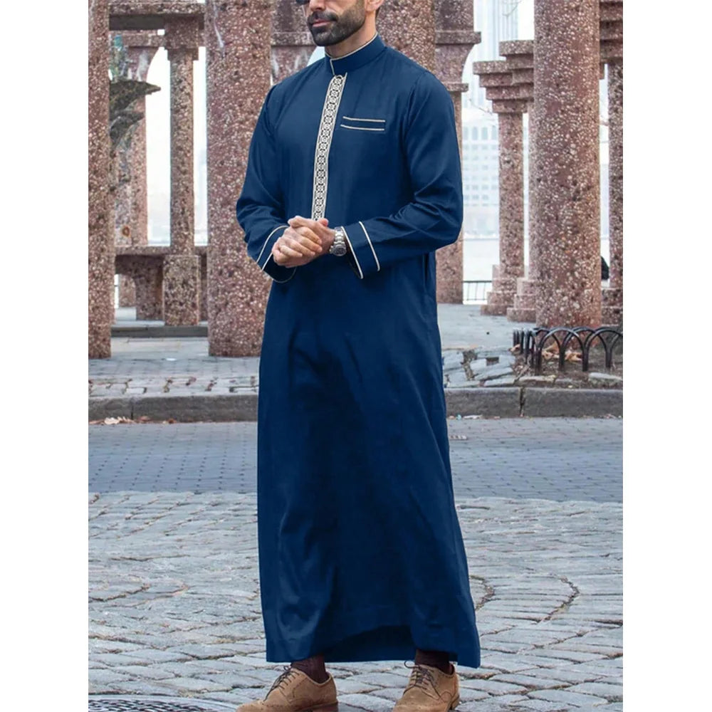Un hombre vistiendo un jubba thobe islámico azul oscuro tradicional con bordados de plata y una pulsera de oro.