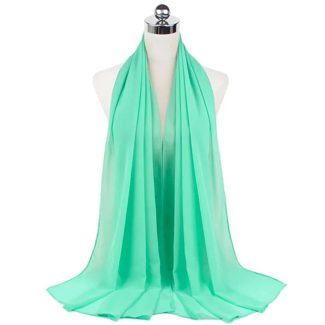 A bright mint green chiffon hijab scarf draped around a mannequin's neck.